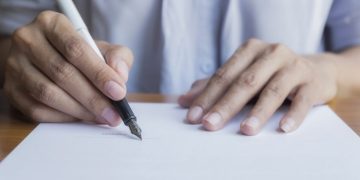 Businessperson Signing Contract,Women writing paper at the desk, man writing with pen and reading books at table,man Signing, Contract, Form. in office ,morning light ,selective focus. 