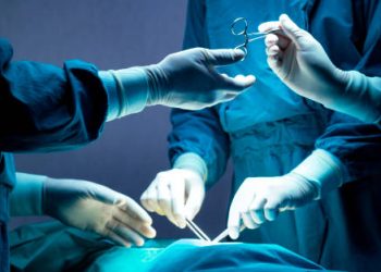 doctor and nurse medical team are performing surgical operation at emergency room in hospital. assistant hands out scissor and instruments to surgeons during operation.