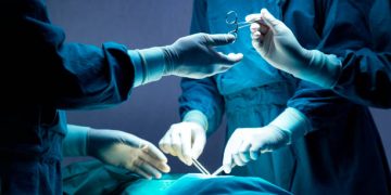 doctor and nurse medical team are performing surgical operation at emergency room in hospital. assistant hands out scissor and instruments to surgeons during operation.