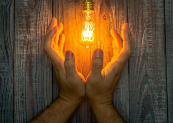 Hand with Glowing bulb on the wood background