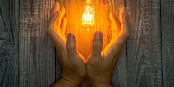 Hand with Glowing bulb on the wood background